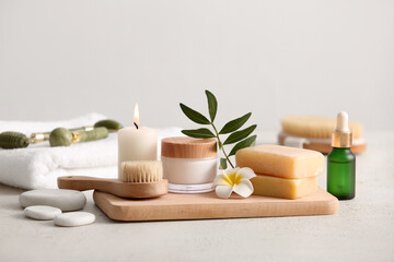 Spa composition with wooden tray, massage body brush, bottle and jar of cosmetic products on beige grunge background, closeup