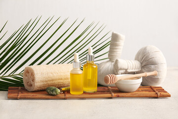 Spa composition with bamboo tray, herbal massage bags and bottles of cosmetic products on white grunge background, closeup