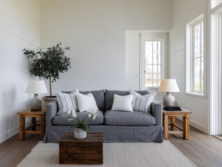 A light-filled living room boasts a cozy gray sofa, accented by natural wood furniture and a lush olive tree.