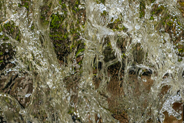 Close-up view of water cascading over moss-covered rocks, highlighting textures, movement, and natural details.