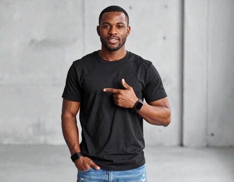 Young man isolated on gray textured wall, smiling while pointing with index finger to black t-shirt, copyspace for advertising