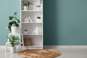 Bookshelf with plants and stool near green wall in room
