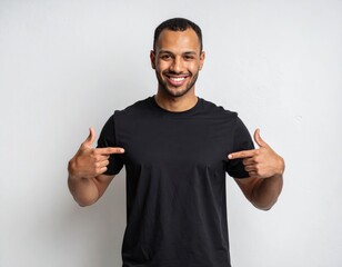 Young man isolated on gray textured wall, smiling while pointing with index finger to black t-shirt, copyspace for advertising