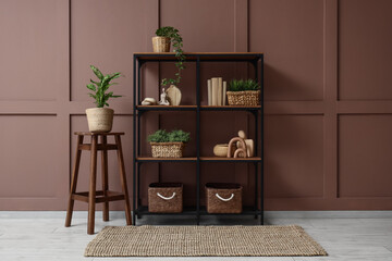 Bookshelf with wicker baskets and plants near brown wall in room
