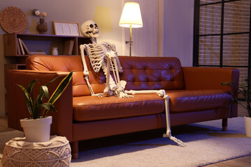 Human skeleton model sitting on leather couch in living room at night