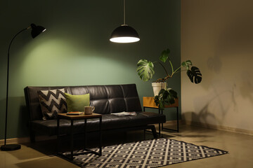 Interior of dark living room with black sofa, table and glowing lamps at night