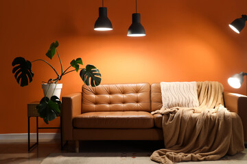 Interior of living room with brown sofa, palm plant and glowing lamps