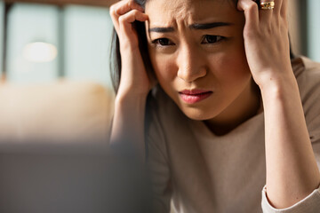 Fototapeta premium Worried self employed woman sits with head in hands, stressed about business project. Female manager overwhelmed by remote work demands, showing emotional fatigue and workplace anxiety at home.