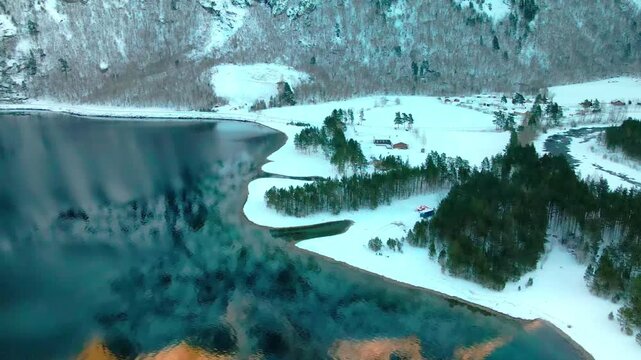 Aerial view capturing the serene winter beauty of a snow covered landscape alongside a tranquil lake, characteristic of the stunning fjords and valleys in Norway, possibly Eresfjord or Eikesdalen.