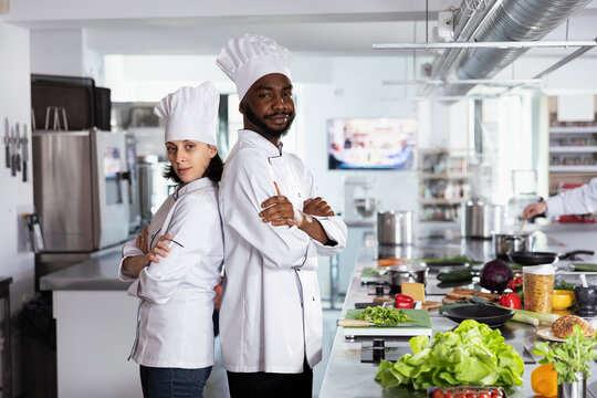 Culinary professionals team in a restaurant kitchen cooking gourmet dishes and carefully preparing ingredients. Chefs in uniform and hat creating the finest gastronomy techniques.