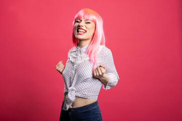 Joyful pink haired woman celebrating success, raising her fists in excitement and smiling brightly...