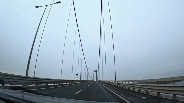 Driving across the braila suspension bridge in romania on a cloudy day. Vehicle crossing the newly built braila suspension bridge over danube river in romania