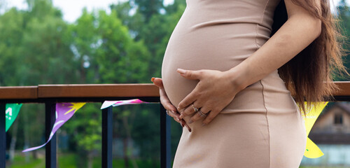 A pregnant woman holding her belly stands on a balcony decorated for a baby shower or gender reveal party, celebrating new life and motherhood. Pregnant woman. Space for inscription. Copy space.