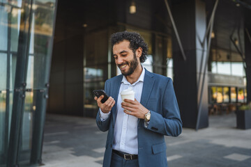 Businessman drinking coffee and reading news on smart phone in front of office building