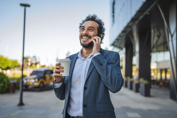 Smiling businessman talking on phone and holding coffee outside office
