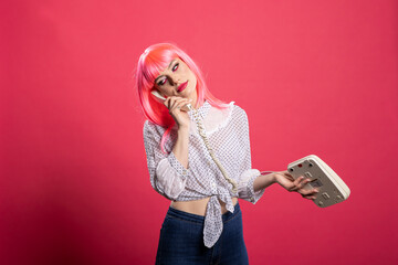 Beautiful caucasian woman with pink hair talking into landline receiver with annoyed expression....