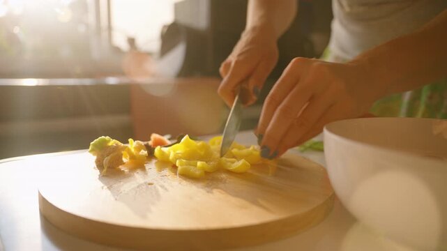 Close-up of Woman Slicing Yellow Bell Pepper with Knife on Wooden Cutting Board in Warm Morning Light, side angle, Healthy Eating Concept