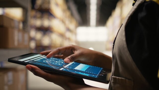 Close up of distribution hub worker overseeing supply chain process for e-commerce. Reviewing logistics and shipping data on tablet, updating tracking labels for order fulfillment. Camera A. - Powered by Adobe