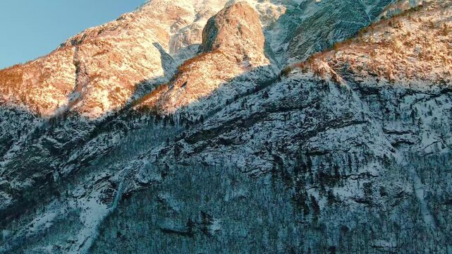 Aerial footage captures the majestic snow capped mountains of Eikesdalen Valley in Norway, bathed in the warm, golden light of sunrise or sunset.