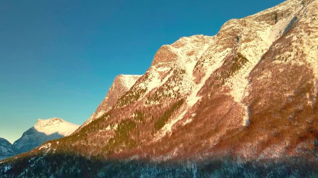 This drone footage snow covered mountains bathed in the warm light of the golden hour, showcasing the stunning natural beauty of Eresfjord or Eikesdalen in Norway.
