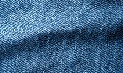 Close-up shot of denim fabric showcasing its texture, weave, and subtle color variations with a diagonal fold creating a shadow effect.  The image highlights the material's inherent details and depth