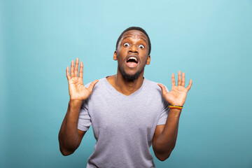 Astonished black male individual looking directly at the camera, raising both his hands in shock....