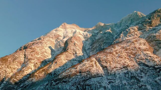 aerial footage capturing the majestic snow covered mountains of Eresfjord or Eikesdalen in Norway, bathed in the warm, golden light of sunrise or sunset.