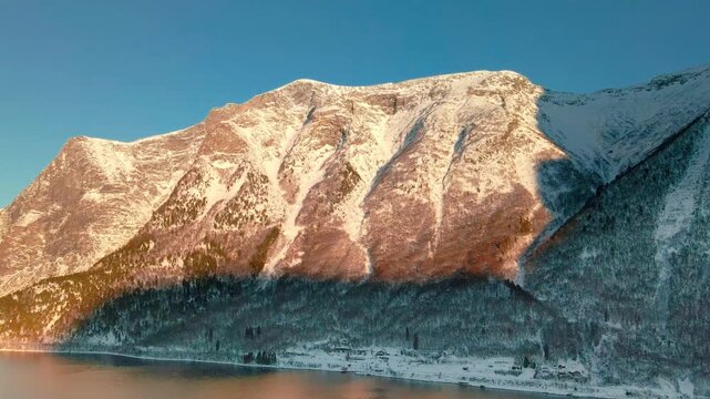 aerial footage capturing the stunning winter beauty of a Norwegian fjord, possibly Eresfjord or Eikesdalen, bathed in the golden light of sunrise or sunset.