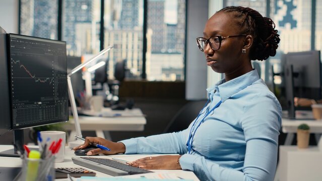 Equity analyst in prop firm office reviews quarterly earnings to assess future stock market value, taking notes. Trader conducts financial analysis to improve investments, writing down info