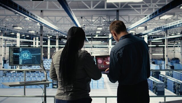 Team of server room technicians alerted by warning message on laptop causing infrastructure slowdowns. Teamworking data center colleagues see malfunction popup caused by software errors, camera A