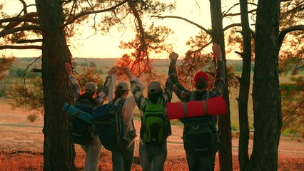 Obraz premium Team of travelers man woman with backpacks, walk through forest raise hands jump have fun sunset sky. Teamwork tourists travelers adventures on vacation. People with backpacks, resting in nature