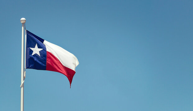 Texas State flag on the pole waving in the wing against bright blue sky 