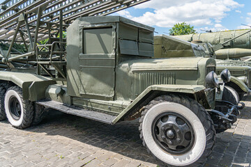 Military vehicle olive green, treaded tires parked on paved surface, likely part of an exhibition...
