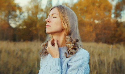 Sick exhausted woman suffering from acute sore in throat flu, touches her neck with hand in autumn