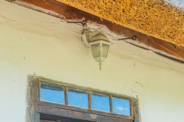 Aged Central European village scene with a closed window reflecting daylight and an off-center lamp...