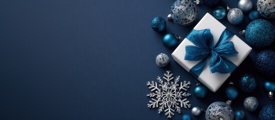 White gift box with blue ribbon surrounded by shiny baubles and silver snowflake decorations on dark blue background creating festive Christmas holiday scene