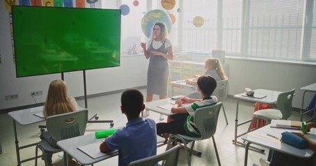 Modern Classroom: Female Teacher Teaching Primary School Children Using Large Digital Screen with Chromakey Mockup. Green Screen Placeholder for Educational Content or Interactive Visuals. Dolly Shot. - Powered by Adobe