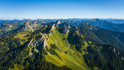 An aerial view captures the majestic beauty of rugged mountain ranges covered in lush green forests and sundrenched alpine meadows under a clear blue sky