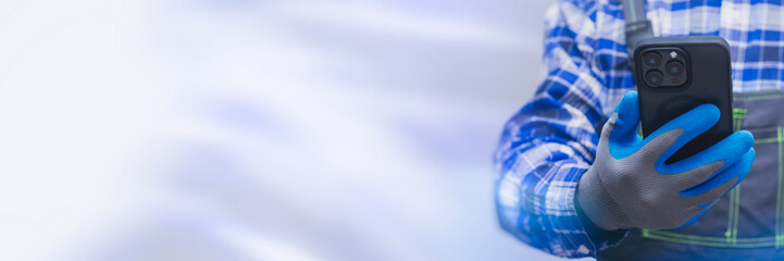 Close-up of a construction worker handyman in protective gloves and workwear using a modern smartphone. Concept digital technology into manual labor and job.