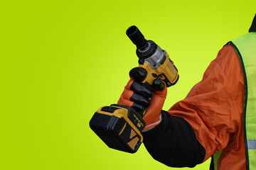 A worker in a protective vest and gloves presses an impact wrench against light green background.