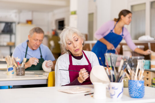 Woman potter with paintbrush, painting on plate in workshop, working in pottery studio