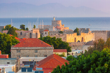 Sunrise view of the Fort of Saint Nicholas in Rhodes, Greece, with medieval walls, lighthouse, and red rooftops in the old town of Rhodes city, Greece