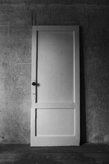 Vintage wooden door with a round knob standing against an old textured concrete wall. Black and white minimal composition with rustic atmosphere