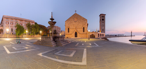 Sunrise view of Evangelismos Church with bell tower and Mandraki Harbour waterfront in Rhodes city, Greece