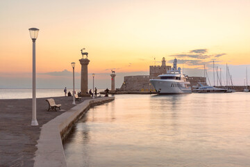 View of Mandraki Harbour with deer statue, lighthouse, yachts and fortress in Rhodes city, Greece at sunset