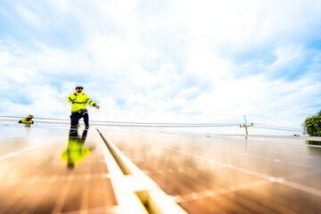 A technician in safety gear inspects solar panels on a metal rooftop, holding a tool. The scene...