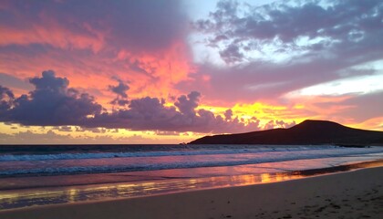 A vibrant sunset paints the sky over a tranquil beach, with waves gently lapping the shore.