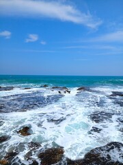 Tropical Rocky Shore with Ocean Waves and Blue Horizon Vertical. Scenic vertical seascape with turquoise ocean waves crashing on rocky beach, perfect travel background.