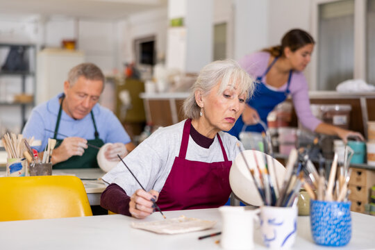 Woman potter with paintbrush, painting on plate in workshop, working in pottery studio