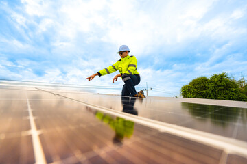 A technician in safety gear inspects solar panels on a metal rooftop, holding a tool. The scene...